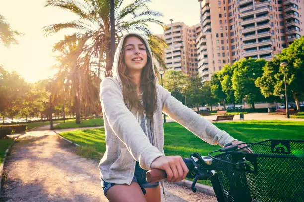 Brunette girl riding bike in the park with hoodie sweater