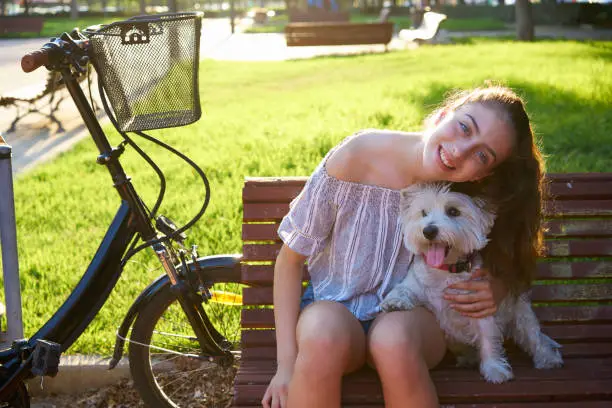 Girl with dog sitting in a park bench with turf grass background outdoor