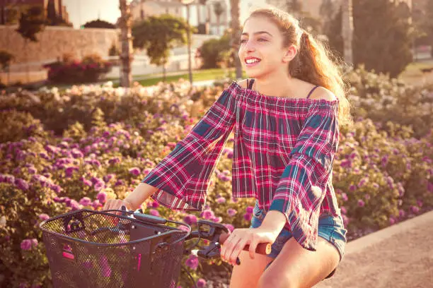 Teen girl riding bicycle in a city flowers park happy