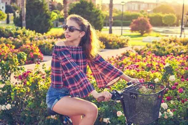 Teen girl riding bicycle in a city flowers park happy