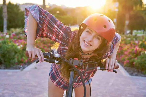 Girl portrait on bicycle with helmet smiling happy at the flowers park outdoor