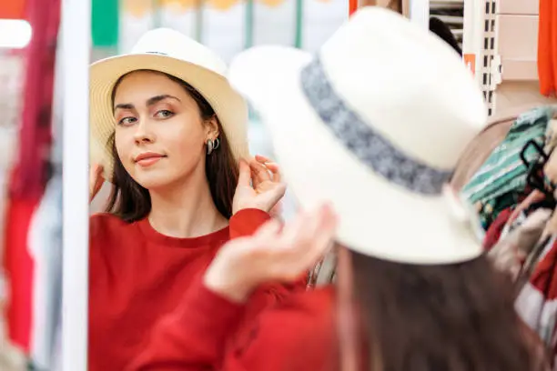 Photo of A young Caucasian woman tries on a straw hat for a vacation, and looks in the mirror. The concept of buying clothes