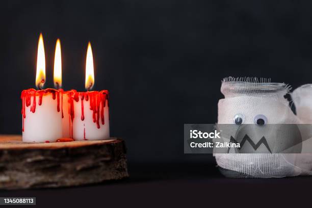 Burning Candles And Mummy From A Jar On Darkness Background White Candles Covered In Red Wax Like Blood Drops Halloween Holiday Concept Stock Photo - Download Image Now