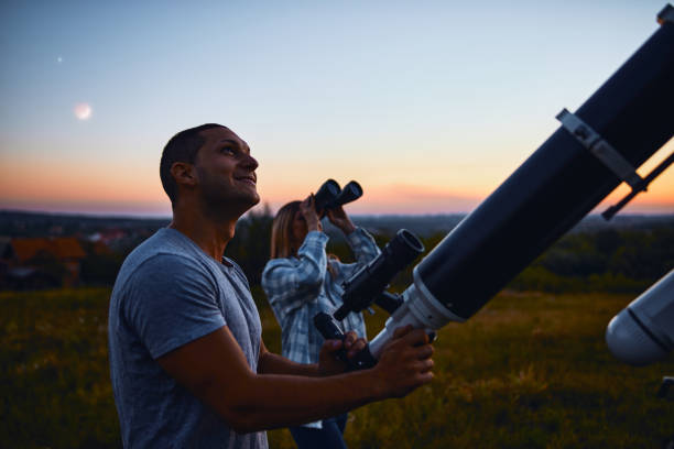 Couple stargazing together with a astronomical telescope.