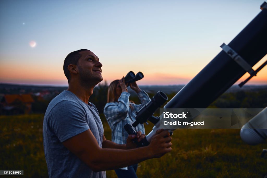 Couple stargazing together with a astronomical telescope. Telescope Stock Photo