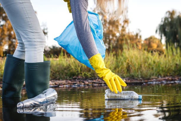 istock water pollution. Volunteer picking up plastic bottle from polluted river 1345092296
