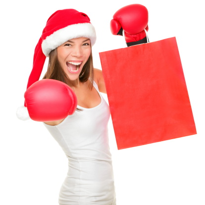Boxing day shopping woman in Santa hat holding shopping bag with copy space. Energetic funny image of beautiful Caucasian / Asian female model isolated on white background. 