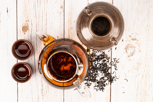 Chinese tea drink in glass pot, tea leaves in clay container and 2 clay tea cups