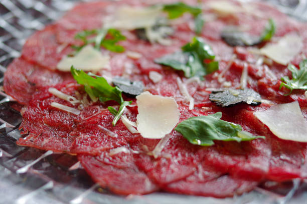 Beef Carpaccio with cheese, black truffle and arugula on round crystal plate close up view