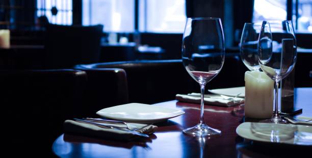 istock Empty wine glasses with white plate, knife and fork on napkin, white candle. Restaurant dinner table setting 1345095078