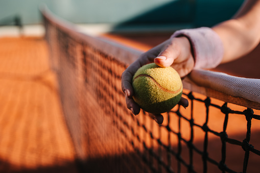 Hand supported by a tennis net holding a tennis ball
