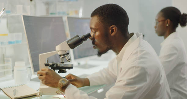 istock African ethnicity scientist with microscope. Team in background 1345098559
