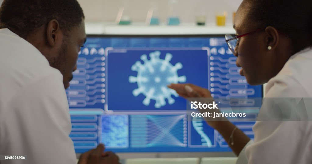 Laboratory equipment and computers. Coronavirus models on screens. African ethnicity scientists discussing. Close up on hands and screens. Pointing details Modern laboratory interior. Studying coronavirus Scientist Stock Photo