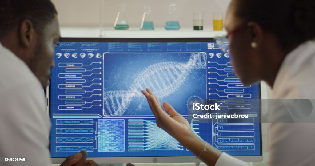 African ethnicity scientists studying DNA samples. Computer screens with DNA sequences. Discussing Scientist examines DNA models in modern Genetic Research Laboratory. DNA Stock Photo