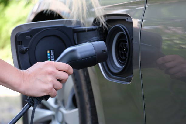 istock Female hand inserts plug for charging electric car closeup 1345100473