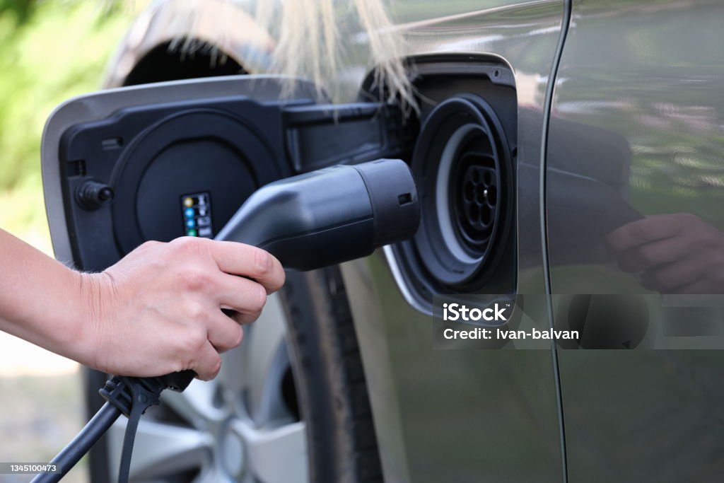 Female hand inserts plug for charging electric car closeup Female hand inserts plug for charging electric car. Fueling hybrid cars concept High Angle View Stock Photo