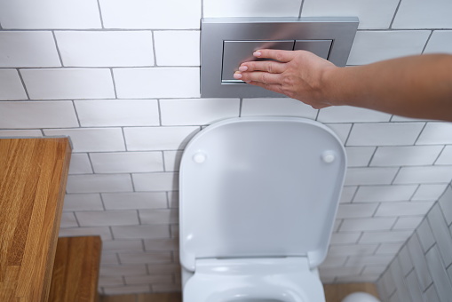 Female hand presses flush button in toilet. Flush cistern button concept
