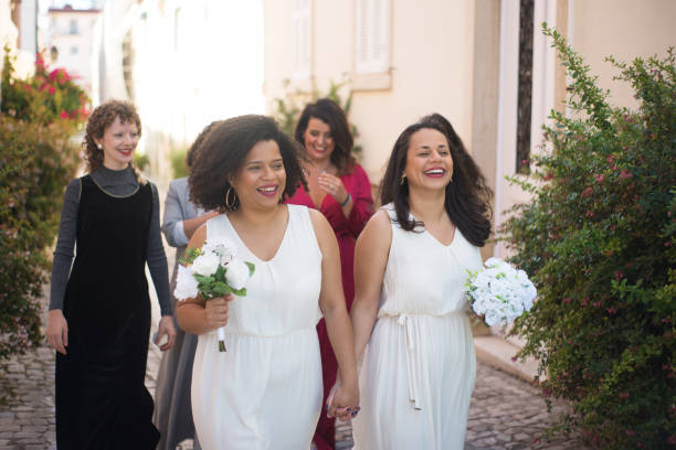 Happy brides and guests at wedding. Smiling women with bouquets holding hands going somewhere. Wedding, LGBT, celebration concept
