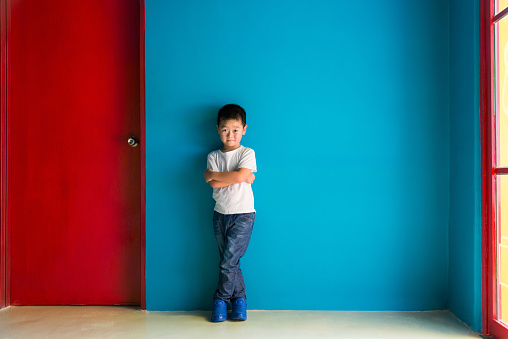 A cute boy standing in front of the blue wall.