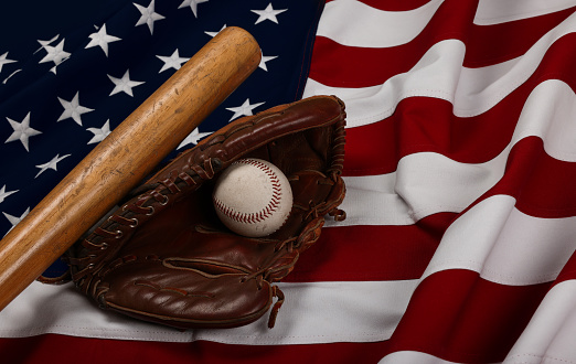 Close up old baseball ball, wooden bat and worn leather vintage glove on American flag background, high angle view