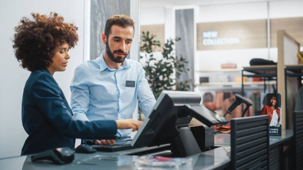 clothing store checkout kasse schalter: weibliche einzelhandels-verkaufsleiterin erklärt neue männliche assistent innisiten alles, was er über die arbeit im modischen shop mit stilvollen markendesigns wissen muss. - supermarket sales clerk retail cashier stock-fotos und bilder