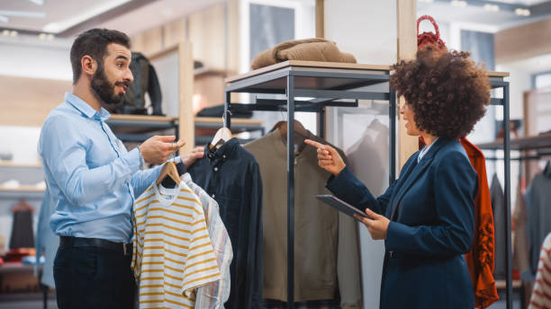 istock Clothing Store: Businesswoman Uses Tablet Computer, Talks to Visual Merchandising Specialist, Collaborate To Create Stylish Collection. Small Business Fashion Shop Sales Manager Talks to Designer. 1345105830