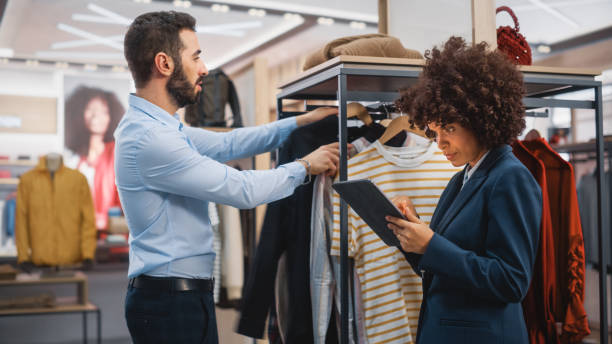 istock Clothing Store: Businesswoman Uses Tablet Computer, Talks to Visual Merchandising Specialist, Collaborate To Create Stylish Collection. Small Business Fashion Shop Sales Manager Talks to Designer. 1345105834