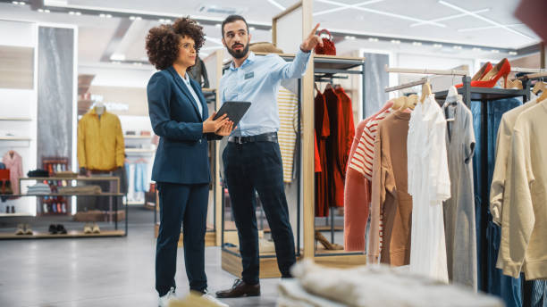 istock Clothing Store: Businesswoman Uses Tablet Computer, Talks to Visual Merchandising Specialist, Collaborate To Create Stylish Collection. Small Business Fashion Shop Sales Manager Talks to Designer. 1345105968