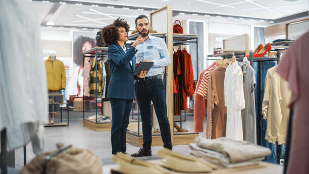 istock Clothing Store: Businesswoman Uses Tablet Computer, Talks to Visual Merchandising Specialist, Collaborate To Create Stylish Collection. Small Business Fashion Shop Sales Manager Talks to Designer. 1345105973
