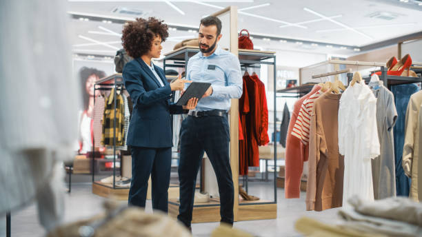 istock Clothing Store: Businesswoman Uses Tablet Computer, Talks to Visual Merchandising Specialist, Collaborate To Create Stylish Collection. Small Business Fashion Shop Sales Manager Talks to Designer. 1345105974