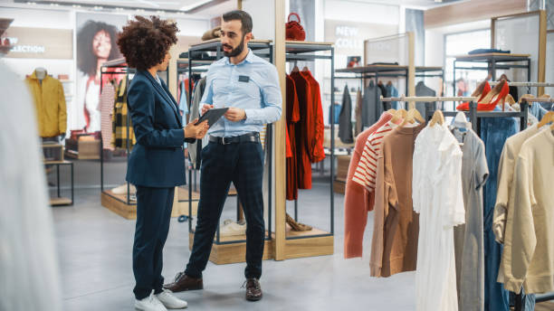 istock Clothing Store: Businesswoman Uses Tablet Computer, Talks to Visual Merchandising Specialist, Collaborate To Create Stylish Collection. Small Business Fashion Shop Sales Manager Talks to Designer. 1345106002
