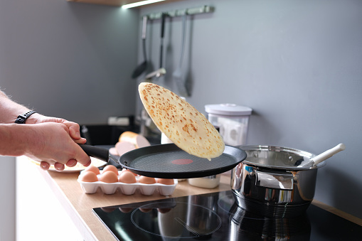 Male chef tossing pancake in frying pan in kitchen closeup