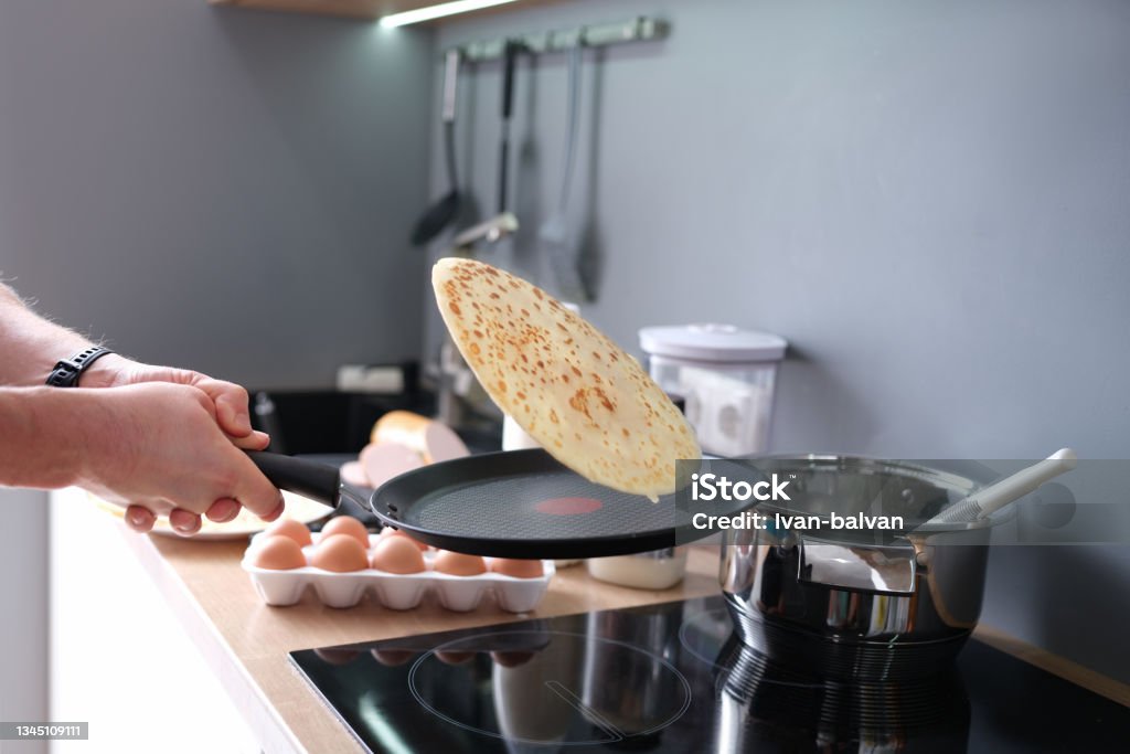 Male chef tossing pancake in frying pan in kitchen closeup Male chef tossing pancake in frying pan in kitchen closeup. Homemade recipes concept Crêpe - Pancake Stock Photo