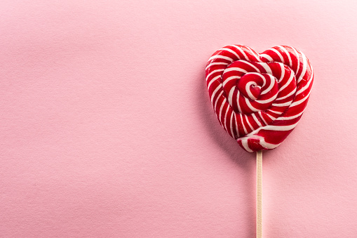 Delicious looking sweet heart-like lollipop stitched on a wooden stick with rose type in background.