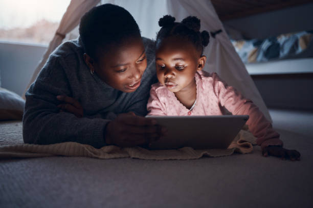デジタルタブレットで娘と就寝時の話を読む母親のショット - digital tablet looking child offspring ストックフォトと画像