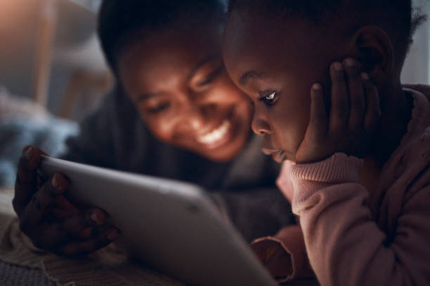 foto de uma mãe lendo histórias de ninar com sua filha em um tablet digital - africa child reading african descent - fotografias e filmes do acervo