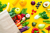 Bag with fruits and vegetables on yellow backdrop