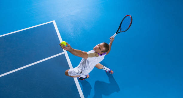 Full-length top view portrait of male professional tennis player serving a ball, training over gym background. During game. Concentration. Portrait of male professional tennis player serving a ball, training over gym background. Concept of active life, team game, energy, sport, competition. Copy space for ad. tennis ball container stock pictures, royalty-free photos & images