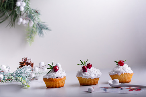Christmas cupcakes with vanilla frosting, cranberries and rosemary on white wooden background. Copy space