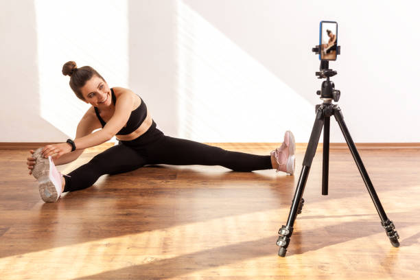 istock Girl coach stretching legs, broadcasting online class, using phone on tripod for recording video. 1345127985