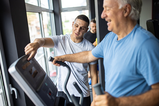 Fitness trainer explaining to senior man how to use treadmill in gym