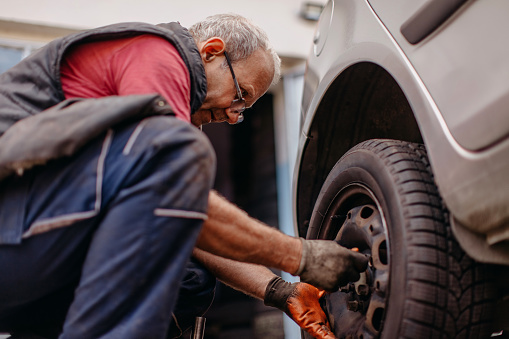 Using pneumatic drill to take of tire on car