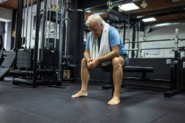 senior man sitting on weight bench and resting after training in health club - weight training weight bench weightlifting men imagens e fotografias de stock