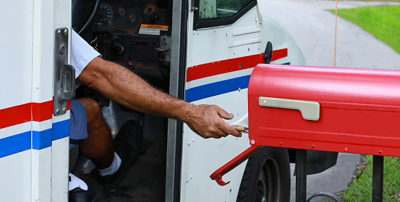 Fort Lauderdale, Florida, USA - October 2, 2021:  Mailman reaches out of his truck to deliver mail.  Official United States mail delivery slowdown started on October 1, 2021.