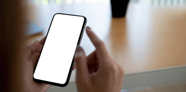 istock Mockup image blank white screen cell phone.women hand holding texting using mobile on desk at home office. 1345137879
