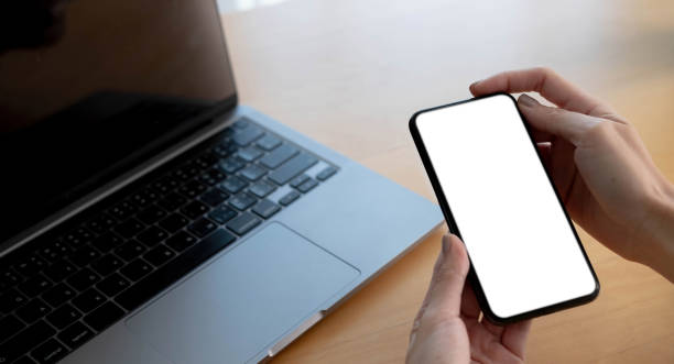 istock Mockup image blank white screen cell phone.women hand holding texting using mobile on desk at home office. 1345137942