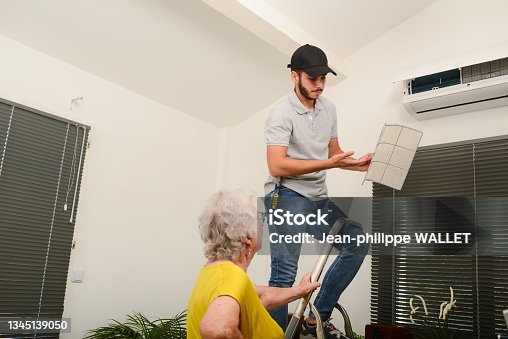 istock handsome young man electrician cleaning air filter on an indoor unit of air conditioning system in client house with senior woman 1345139050