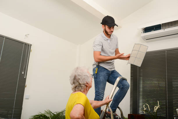 handsome young man electrician cleaning air filter on an indoor unit of air conditioning system in client house with senior woman - manual worker fotos imagens e fotografias de stock