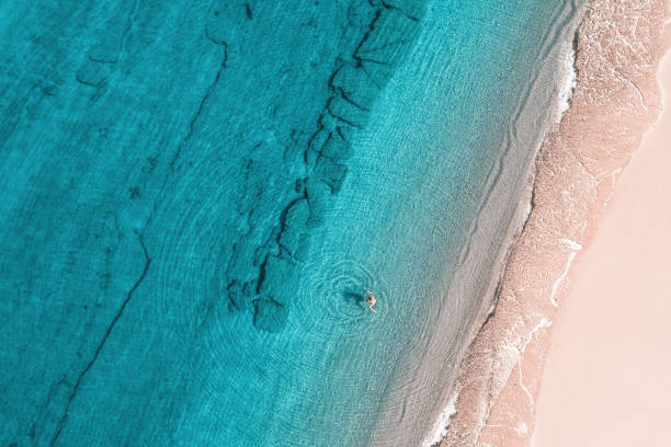 junge frau im bikini, die im meerwasser am strand schwimmt. blick von oben. oben, drohnenansicht - sea swimming greece women stock-fotos und bilder