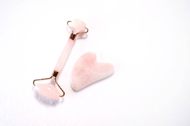 istock Pink face roller and gua sha massager made from natural quartz  stone over white background with drops .  Lifting and toning treatment at home. 1345144084